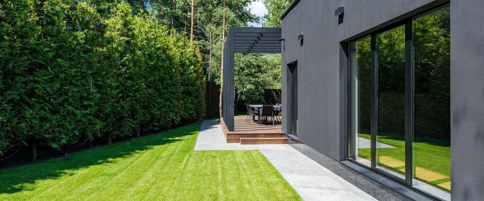 Modern dark-clad house with a long glazed wall beside a lawn